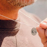 A man wears a sterling silver charm necklace engraved with a mountain peak