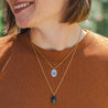 A woman wears a 14k gold charm necklace personalized with her name as an engraved monogram