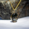 Natural black granite stone set as a necklace in a 14k gold fill setting. The original stone is visible in the background.