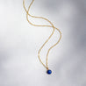 A small, round stone pendant made from natural blue rock. It hangs from a long/short 14k gold chain.